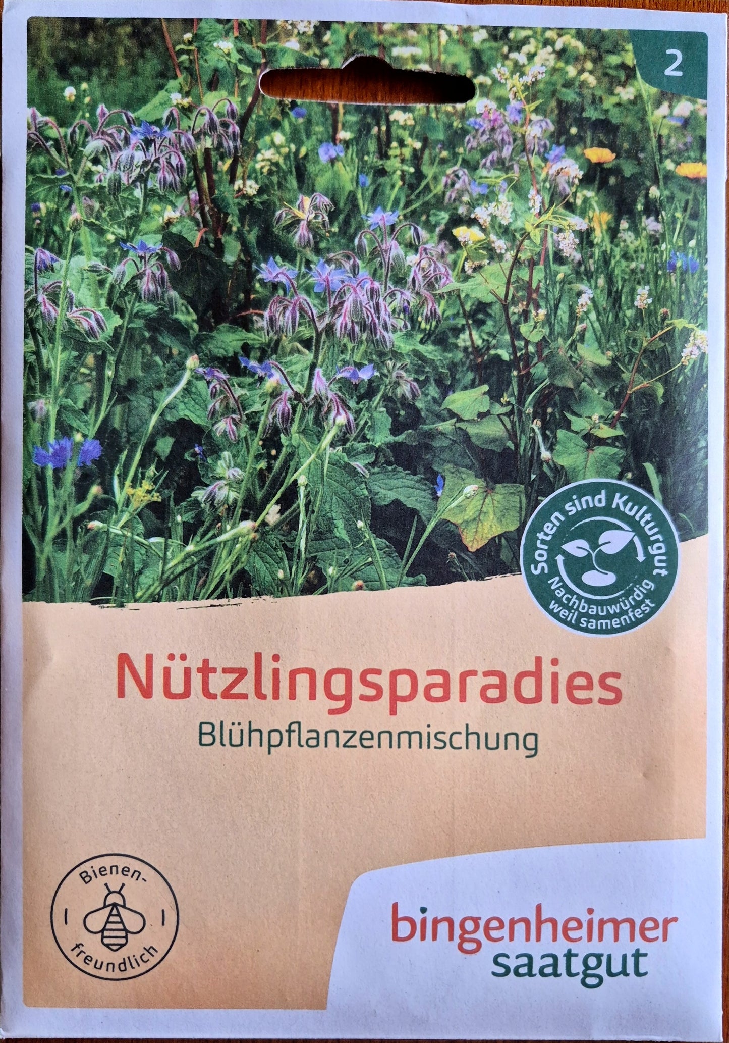 verpackung_wildblumen_wiese.jpg - Verpackung der Nützlingsparadies-Saatgutmischung von Bingenheimer Saatgut mit einem blühenden Wildblumenbeet als Beispiel für den Wachstumserfolg.